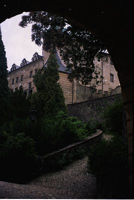 Historic stone castle framed by dense foliage, illuminated by soft evening light. Gothic-style architecture with steep gables...