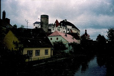 Vintage sepia-toned riverside town with historic European architecture. Prominent brick chimney and red-roofed buildings fram...