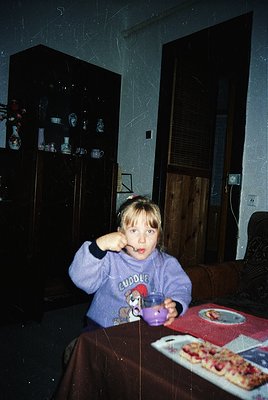 Young child in a 1990s-style "Cuddle" hoodie poses at a table with a small cup, likely for a drink or snack. Background featu...