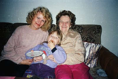 Family portrait featuring two women and a child on a patterned sofa, likely 1990s. The adult on left wears a light pink sweat...