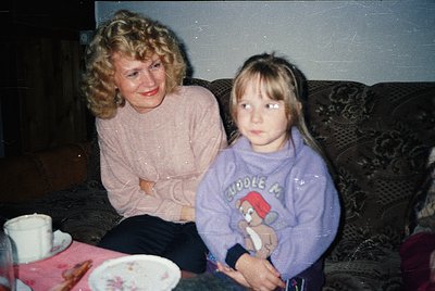 Vintage indoor portrait of a woman and child on a floral-patterned sofa, 1980s-90s. Woman wears a pink sweater; child holds a...