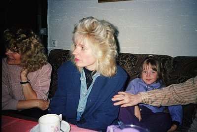 Vintage indoor portrait of three women in a dimly lit room, likely 1970s–1980s. The woman in the center wears a voluminous bl...