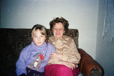 Vintage indoor portrait of a grandmother and young girl on a patterned armchair, likely 1980s–1990s. The girl wears a purple ...