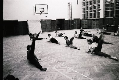 Indoor gymnasium scene featuring a group exercise session, likely from the 1960s–1970s. Participants perform floor exercises ...
