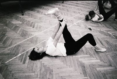 Vintage black-and-white photo of a dynamic floor exercise in a gymnasium, likely mid-20th century. A person performs a split ...