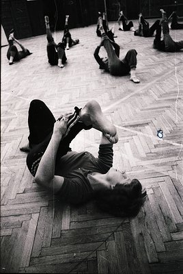 Group fitness class in a gymnasium, 1960s–1970s. Participants perform floor exercises in coordinated poses, emphasizing flexi...