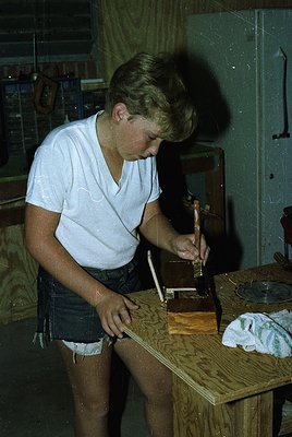 Vintage black-and-white photo of a young man operating a manual typewriter in a dimly lit workshop. Wooden workbench, vintage...