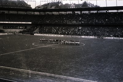 Black-and-white stadium shot showing a pre-match ceremony with teams lined up on the field, likely 1960s–1970s. Multi-tiered ...