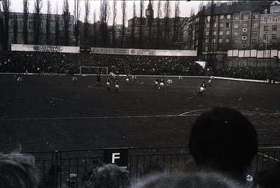 Black-and-white shot of a packed stadium during a 1960s–70s soccer match, likely in Czechoslovakia ( ). Crowds fill stands be...