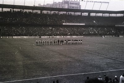 Black-and-white stadium photo showing two football teams in pre-match formation, 1960s-70s. Teams stand on a grass pitch with...