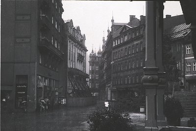 Mid-20th century European street scene featuring Gothic Revival architecture with steep gables, ornate facades, and wrought-i...