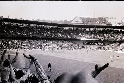 Vintage black-and-white stadium shot showing packed stands with spectators raising arms in celebration. Prominent "Renault" a...