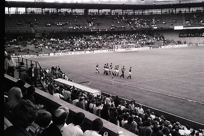 Black-and-white stadium shot showing a mid-20th-century football match. Players in vintage striped jerseys line up for kickof...