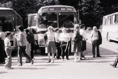 A group of people boarding a vintage **Zajezd** bus (likely Eastern European, mid-20th century) in an outdoor setting. Casual...