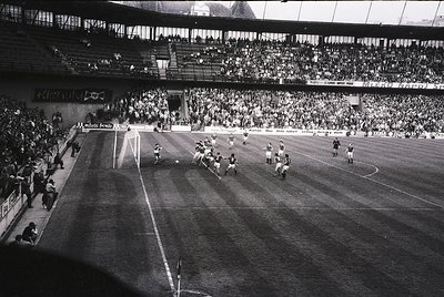 Black-and-white shot of a packed stadium during a high-stakes soccer match, likely 1960s–1970s. Crowds fill tiered stands, wh...