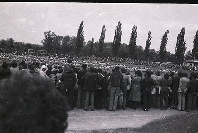 Black-and-white stadium shot of dense crowd facing a soccer field, likely mid-20th century. Uniform attire suggests organized...