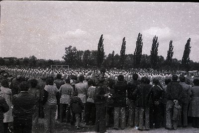 Crowd of people gathered outdoors in a formal, organized procession, likely a funeral or memorial. Uniform attire suggests a ...