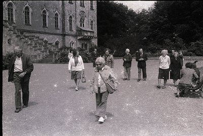 Gothic-style building with pointed arches and stone detailing, mid-20th century. Group of elderly individuals in casual 1960s...