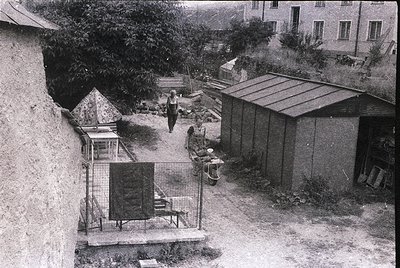 Aerial view of a courtyard with mid-20th-century urban housing. Concrete walls, metal-fenced utility area with a small cage-l...