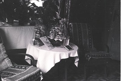Vintage indoor still-life featuring a small round table draped in a white cloth, adorned with a tiered cake stand holding a l...