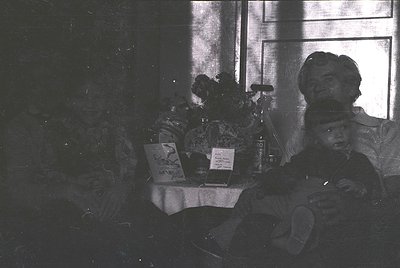 Vintage black-and-white interior shot of a seated man in a military uniform, likely 1940s–1950s. Table beside him holds a boo...
