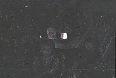 Vintage low-light portrait of two individuals in patterned headscarves, likely Eastern European or Middle Eastern. Blurred bu...