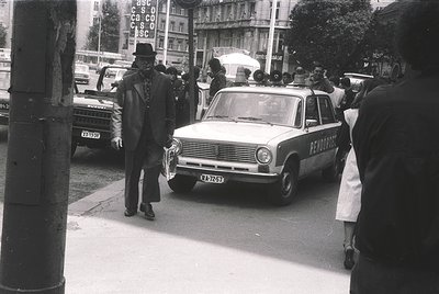 Vintage black-and-white street scene featuring a **1960s-era ambulance** (marked "ПЕРВАЙНА ПОМОЩ" in Cyrillic) parked on a bu...