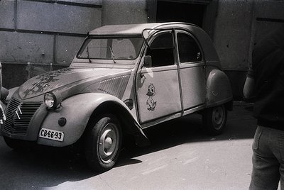 Classic Citroën 2CV with vintage French maritime decals, parked beside a concrete wall. Distinctive rounded body, small wheel...