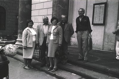 Black-and-white group portrait in front of a stone building, likely from the 1960s–1970s. Five adults pose formally, dressed ...