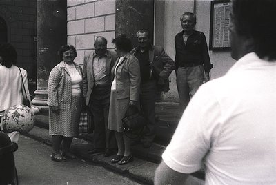 Group of six adults posing outside a building with classical architectural details, likely mid-20th century. Men wear suits/v...