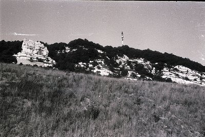 Vintage black-and-white coastal landscape featuring rugged limestone cliffs and a tall lighthouse on a hilltop. Dense vegetat...