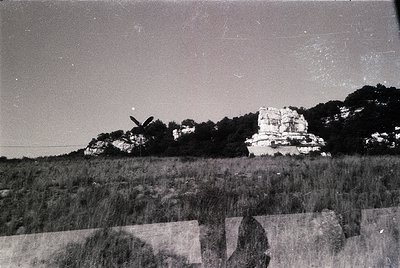 Vintage black-and-white aerial view of rugged, eroded rock formations in a grassy plain. Distinctive layered cliffs and isola...