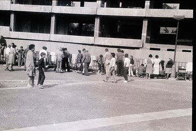 Crowd of people lined up outside a Soviet-era concrete apartment block, likely for rationed goods or public services. Mid-20t...