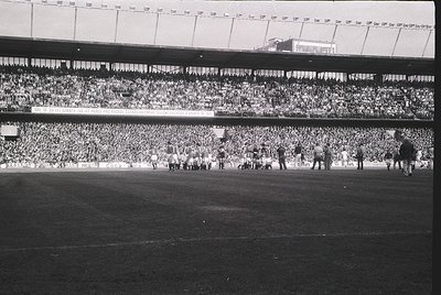 Vintage black-and-white stadium shot showing packed stands with dense crowds, likely UEFA/European Cup final. Players in whit...