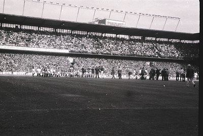 Vintage black-and-white stadium shot showing packed tiered seating with dense crowds, likely a 1950s–1960s European football ...