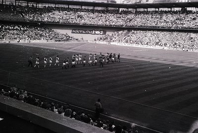 Black-and-white stadium shot showing a pre-game ceremony with teams lined up on the field, likely mid-20th century. Massive c...