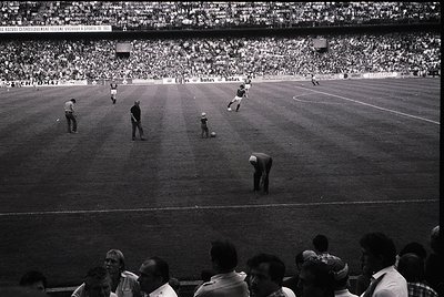 Vintage black-and-white soccer match in a packed stadium, featuring midfield action with players in classic striped jerseys. ...
