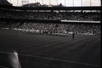 Black-and-white stadium shot showing a pre-game ceremony with athletes in formation, likely 1960s–1970s. Crowd fills tiered s...