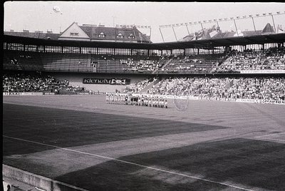 Black-and-white stadium shot featuring a large crowd in tiered seating, likely from the 1950s–1960s. Prominent "Kienzl" signa...