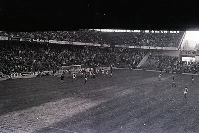 Black-and-white shot of a packed stadium during a nighttime soccer match, featuring a packed stadium with floodlit field and ...