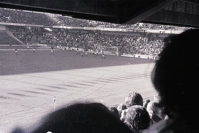 Black-and-white stadium shot showing packed stands with visible scoreboard reading "1-0" and "C.S. Steaua." Crowd fills tiere...