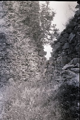 Black-and-white shot of rugged, weathered rock face with sparse vegetation. Vertical stone wall on right, likely a cliff or q...