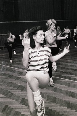 Vintage black-and-white photo of women practicing rhythmic gymnastics in a gymnasium, 1960s-70s. Wooden floor, striped leotar...