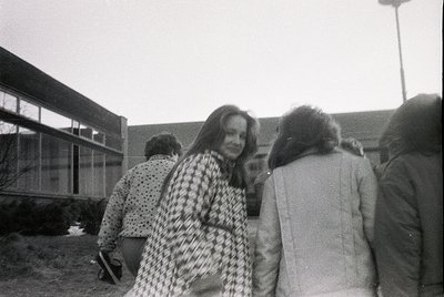 Black-and-white candid of a group in 1970s outdoor setting, likely Eastern Europe. Woman in foreground wears a polka-dot coat...