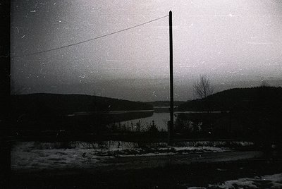 Vintage black-and-white winter landscape featuring a lone utility pole framing a frozen lake and forested horizon. Snow blank...
