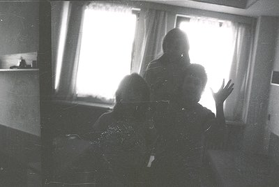 Silhouetted figures in a dimly lit interior, framed by sunlight streaming through curtains. Likely mid-20th century based on ...