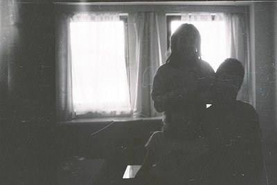 Silhouetted mother and child seated indoors, backlit by natural light through sheer curtains. Vintage black-and-white composi...