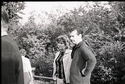 Black-and-white candid shot of three individuals in a wooded area, likely mid-20th century. Central figures wear striped blaz...