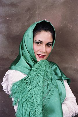 Portrait of a woman in traditional Middle Eastern attire, featuring a green lace headscarf and draped shawl over a white blou...