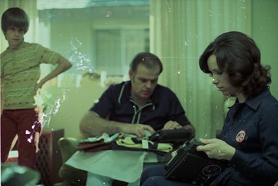 Vintage indoor scene featuring three individuals seated at a table with a typewriter. Man in striped shirt and woman in dark ...